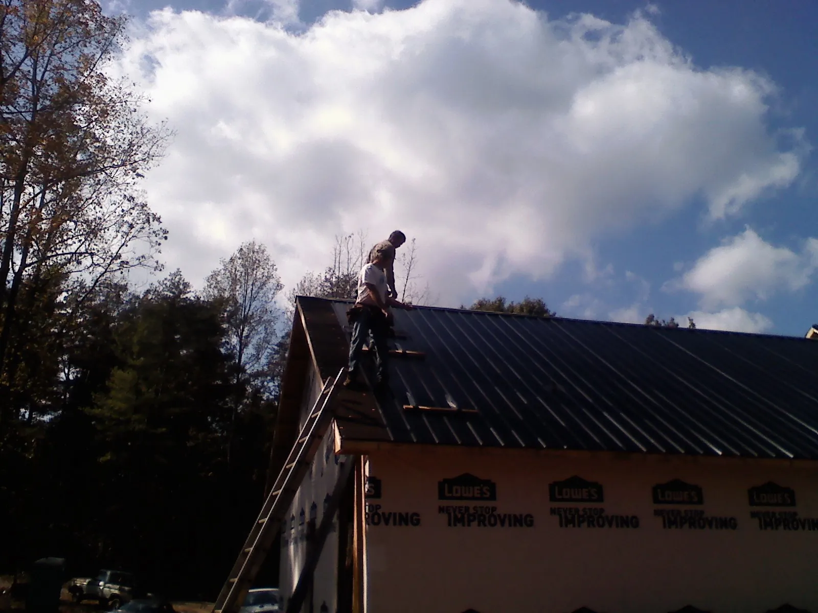 Roofer fastening dark metal panels high against a cloudy sky, from a Roof Inspection job in Hamlet