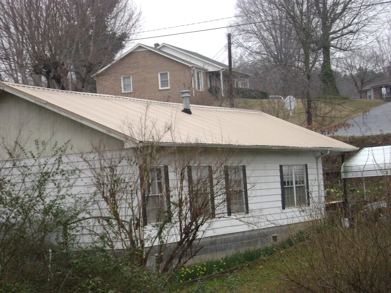 Tan metal roof on a white sided house set into a hillside — Commercial Roofing by Roofing Brothers in Hamlet