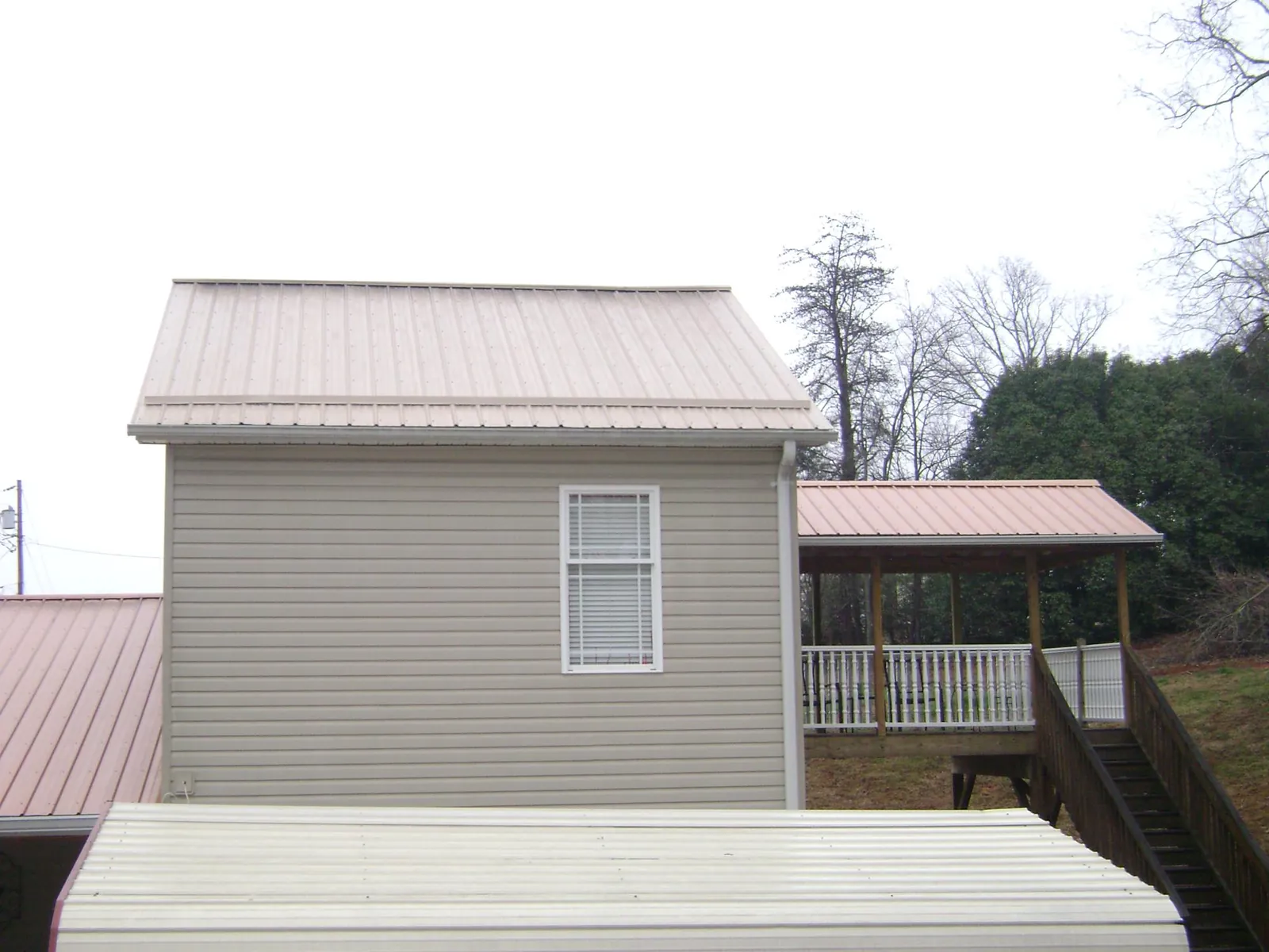 Tan metal roofs on a two story addition and attached porch, from a Roof Replacement job in Hamlet